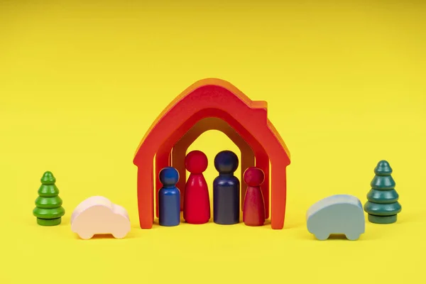 Wooden figures, miniature people standing inside colorful house on yellow background. Family with children, stay home, real estate concept