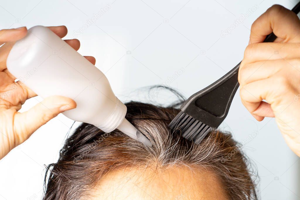 Closeup woman hands dyeing hair using black brush. Middle age woman colouring dark hair with gray roots at home