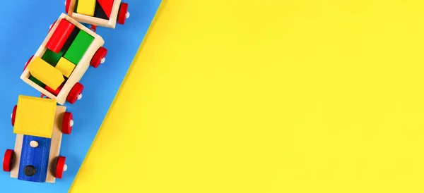 Kinderspeelgoed achtergrond. Houten speelgoedtrein met kleurrijke blokken op lichtblauwe en gele achtergrond. Bovenaanzicht — Stockfoto