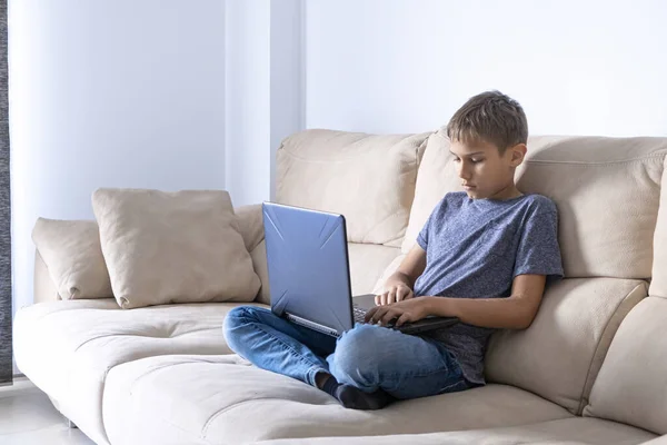 少年はノートパソコンで宿題をして、家でビデオを見ている。技術、教育、子供のためのオンライン遠隔学習。ホームエンターテイメントに滞在する — ストック写真