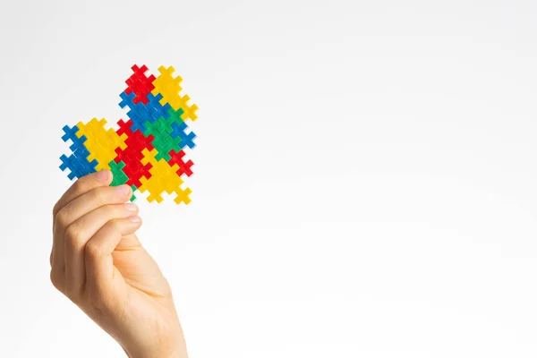 Az autizmus világnapja koncepció. Gyermek kéz gazdaság színes puzzle szív fehér háttér — Stock Fotó