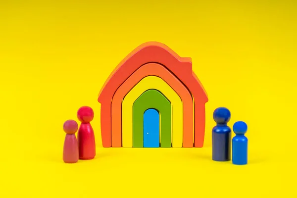 Figuras de madera, personas en miniatura de pie frente a la casa de color arco iris sobre fondo amarillo. Divorcio, conflicto entre padres, custodia de hijos después del divorcio — Foto de Stock