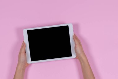 Eller pastel pembe arka planda dijital tablet bilgisayarı tutuyor