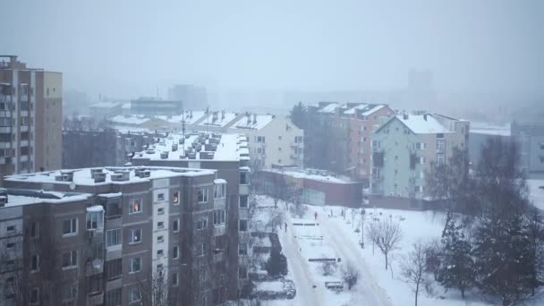 Blick aus dem Fenster eines mehrstöckigen Gebäudes auf die Stadt am Wintertag bei Schneefall. Verschneiter bewölkter Tag, Menschen draußen. 4k Videomaterial — Stockvideo