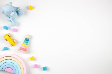 Bebek oyuncakları beyaz arka planda çerçevelenmiş. Oyuncak ayı ve tahta oyuncaklar masanın üstünde. Üst görünüm