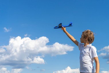 Açık havada güneşli bir günde mavi gökyüzüne karşı mavi oyuncak uçakla oynayan çocuk.