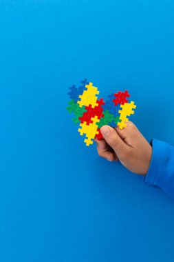 Dünya otizm farkındalık günü konsepti. Açık mavi arkaplanda renkli yapboz kalbini tutan çocuk eli