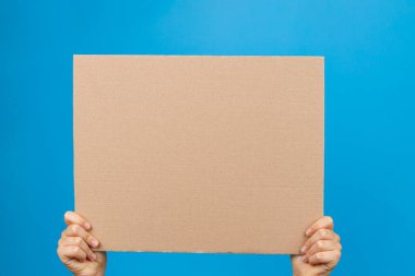 Mavi arka planda boş kahverengi karton poster tutan eller
