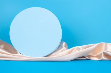 Açık mavi zemin üzerinde Geometrik podyum ve örtülü şampanya rengi ipek kumaş. Kozmetik ürün sunumu için boş vitrin, tanıtım satışı