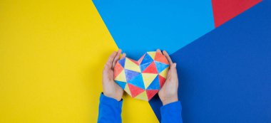 Çocuk elleri renkli kağıt kalbi çok renkli kağıtların üzerinde tutuyorlar. Dünya otizm farkındalık günü konsepti