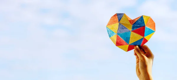 Mano de niño sosteniendo el corazón colorido sobre fondo azul del cielo. Concepto del Día Mundial de la Conciencia del autismo —  Fotos de Stock