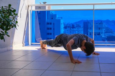 Çocuk balkonda şınav çekiyor spor egzersizleri yapıyor. Spor, sağlıklı yaşam tarzı, eğitim, evde boş vakit geçirme.