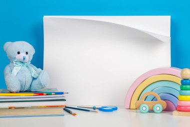Oyuncak bebekler, oyuncak ayılar, kitaplar, okul malzemeleri ve beyaz masadaki büyük boş defterler. Okula, eğitime, anaokuluna, anaokuluna.
