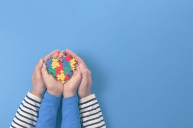 Dünya otizm farkındalık günü konsepti. Yetişkin ve çocuk elleri açık mavi arka planda yapboz kalbini tutuyor