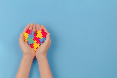 Açık mavi arka planda renkli kalbi tutan bir çocuk. Dünya otizm farkındalık günü konsepti