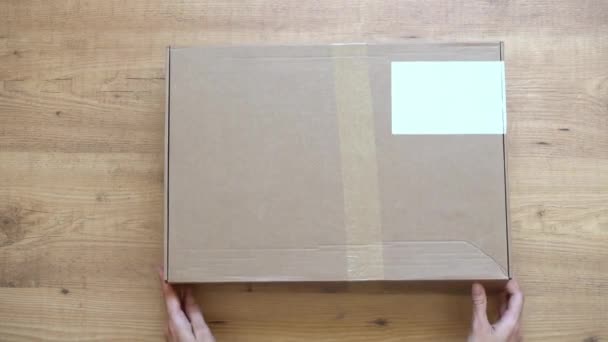 Online shopping. Kvinde hænder åbning, udpakning udpakning nyt pap med flere tøj på træbord. Top down visning – Stock-video