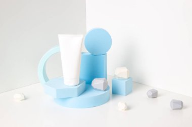 Bir boş kozmetik tüp ve açık mavi geometrik şekillerle soyut arka plan modası kompozisyonu, beyaz arkaplan üzerinde ürün sunumu için platform biçiminde podyum oluşturur