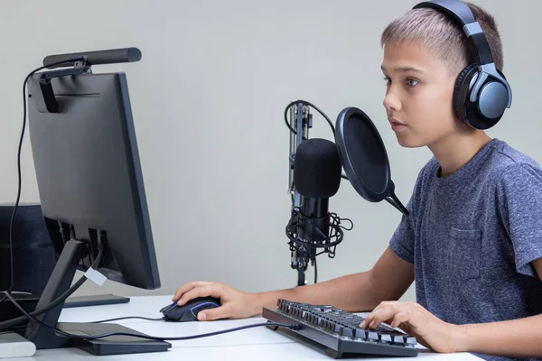 Online learning, remote education, gaming, school concept. Teenage boy wearing headphones using microphone playing video games online on computer, recording podcast, online learning from home.