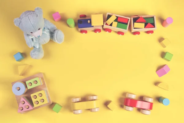 Baby kids educational toys background. Teddy bear, wooden train, car, colorful wood toys and bricks on pastel yellow background. Top view, flat lay