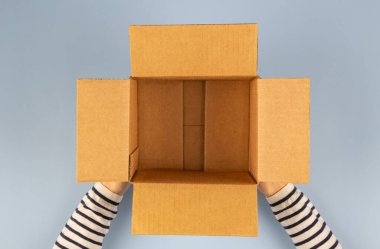 Female hands with empty open cardboard box on light gray background. Top view