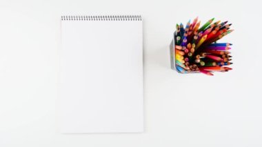 Boş spiral çizim defteri ve beyaz masa üst manzaralı bir sürü renkli kalemli metal kalem tutacağı. Hareket animasyonunu durdur. 4K