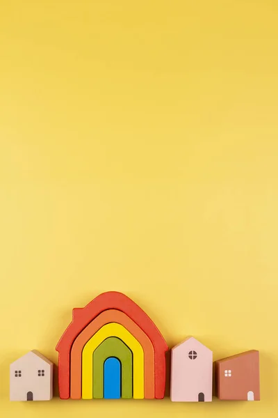 Kis pasztell színű faházak és szivárvány zászlós játék ház sárga háttér — Stock Fotó