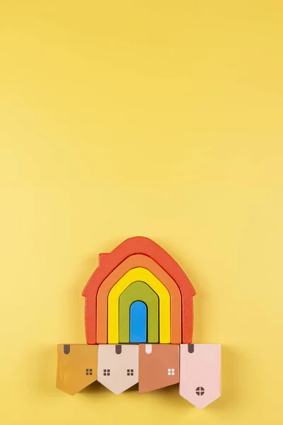 Arco-íris bandeira casa de brinquedos e pequenas casas de madeira cor pastel abaixo no fundo amarelo — Fotografia de Stock