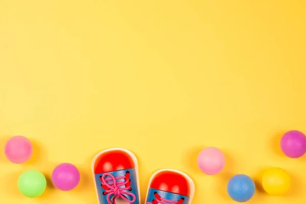 Sapatos de brinquedo educativos de madeira e bolas coloridas no fundo amarelo pastel. Vista superior — Fotografia de Stock
