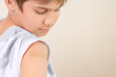 Aşı sonrası kolunda bandaj bandı olan genç bir çocuk. Covid aşısı, çocuklar ve gençler için sağlık hizmetleri