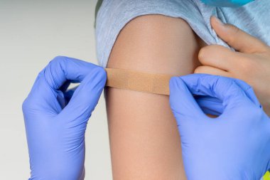 Lastik koruyucu eldivenli hemşire aşıdan sonra koluna bandaj yapıştırıyor. Enjeksiyon covid aşısı