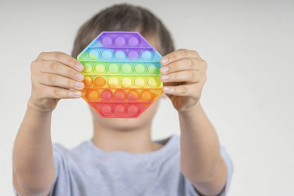 Boy holding sensory pop it fidget toy in his hands. Push pop-it fidgeting game helps relieve stress, anxiety, autism, provide sensory and tactile experience for children