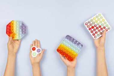 Bir çok el mavi arka planda hareketli oyuncaklar tutuyor. Pop-it kıpır kıpır oyunu stresi, endişeyi, otizmi azaltır, çocuklara duyusal ve dokunsal deneyim sağlar