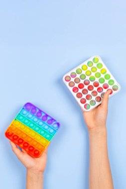 Çocukların elleri mavi arka planda hareketli oyuncaklar tutuyor. Pop-it kıpır kıpır oyunu stresi, endişeyi, otizmi azaltır, çocuklara duyusal ve dokunsal deneyim sağlar