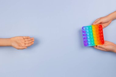 Çocukların elleri mavi arka planda yeni moda pop müziği oyuncağını alır ve verir. Pop-it kıpır kıpır oyunu stresi, endişeyi, otizmi azaltır, çocuklara duyusal ve dokunsal deneyim sağlar