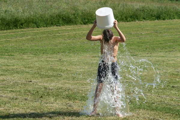 Teenage boy pouring bucket of cold water over his head outdoors. Ice water challenge. Cold water therapy benefits