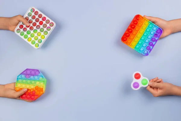 Wiele rąk trzyma kolorowe pop to fidget zabawki na niebieskim tle. Push pop-it fidgeting gra pomaga złagodzić stres, lęk, autyzm, zapewnić wrażenia sensoryczne i dotykowe dla dzieci — Zdjęcie stockowe