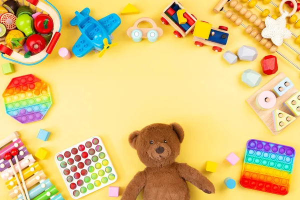 Baby barn leksak ram med nalle, trä och musikaliska leksaker, abacus, plan, pop det fidget leksaker och färgglada block på gul bakgrund. Ovanifrån, platt ligg — Stockfoto