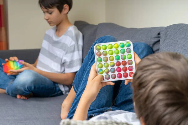 Nastoletni chłopcy bawią się tęczowymi zabawkami w domu. Push pop-it fidgeting gra pomaga złagodzić stres, lęk, autyzm, zapewnić wrażenia sensoryczne i dotykowe dla dzieci. — Zdjęcie stockowe
