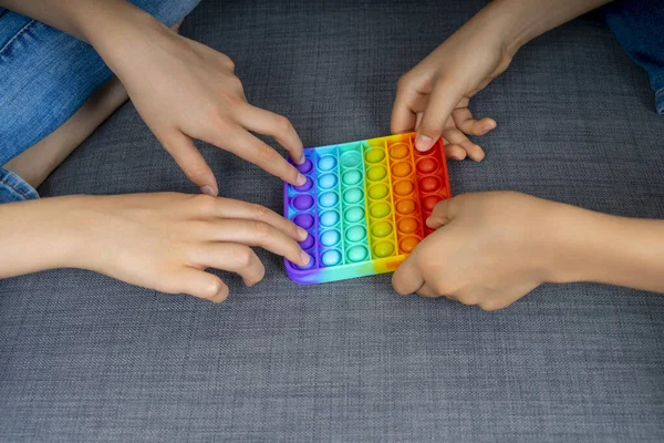 Close up kids hands playing with rainbow pop-it fidget toys at home. Push pop-it fidgeting game helps relieve stress, anxiety, autism, provide sensory and tactile experience for children