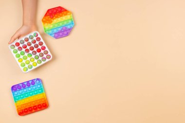 El ele tutuşan çocuk pastel arka planda hareketli oyuncağı tutuyor. Pop-it kıpır kıpır oyunu stresi, endişeyi azaltmaya, çocuklara duyusal ve dokunsal deneyim kazandırmaya yardımcı olur