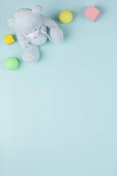 Дитячий іграшковий фон з плюшевим ведмедем, дерев'яними блоками та різнокольоровими кульками на світло-блакитному фоні. Вид зверху, плоский ліжко — стокове фото