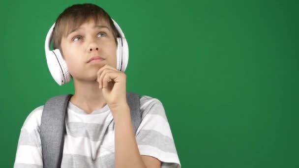 年轻英俊的男孩，带着耳机和背包，在绿色屏幕上的彩色背景下思考。4k视频 — 图库视频影像