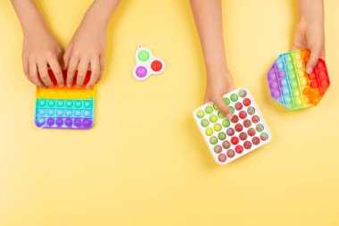 El ele tutuşup, sarı arka planda oynaşan oyuncaklar yapıyorlar. Pop-it kıpır kıpır oyunu stresi, endişeyi azaltmaya, çocuklara duyusal ve dokunsal deneyim kazandırmaya yardımcı olur