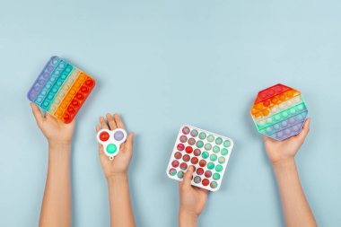 Birçok el mavi arka planda hareketli oyuncakları tutuyor. Pop-it kıpır kıpır oyunu stresi, endişeyi, otizmi azaltır, çocuklara duyusal ve dokunsal deneyim sağlar