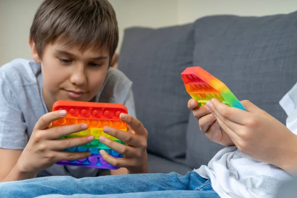 Kids playing with rainbow pop-it fidget toys at home. Push pop it fidgeting game helps relieve stress, anxiety, provide sensory and tactile experience for children