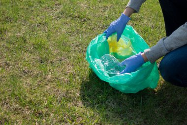 Çöplerin doğasını temizleyen kadın. Mavi eldivenli gönüllü eller çöpleri plastik torbaya dolduruyor. Gönüllü olmak, kirlilik, ekoloji ve plastik konsept