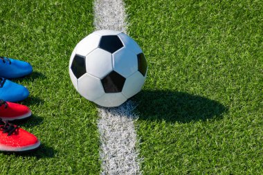 Futbol geçmişi var. Suni sahada futbol topu ve iki çift futbol ayakkabısı.