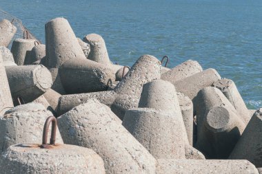 Beton tetrapod dalgaları kıyı boyunca uzanır. Kıyı dalgaları, deniz suyu arka planındaki büyük dalgalardan korunuyor.