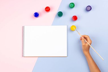 Boş bir çizim defterinde boya fırçası resmi olan çocuk eli. Yaratıcı sanat eserlerine en iyi bakış açısı masa başında suluboya bıyık sağlar. Okula dönmek, öğrenmek, çocuklar ve gençler için boş zaman.