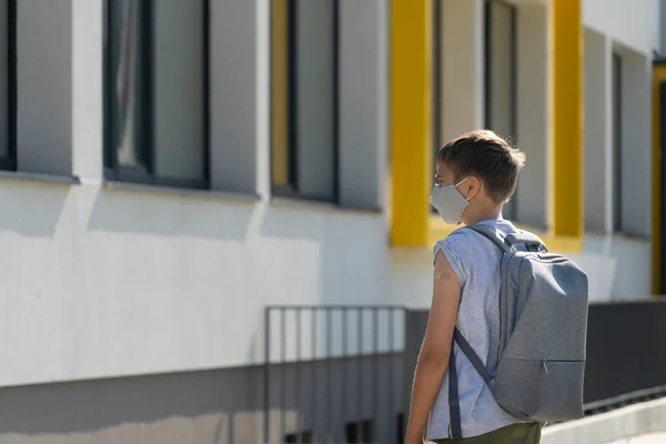 Εφηβικό αγόρι σε προστατευτική μάσκα με αυτοκόλλητο γύψο επίδεσμο στο χέρι του χαρούμενος πίσω στο σχολείο μετά τις καλοκαιρινές διακοπές — Φωτογραφία Αρχείου